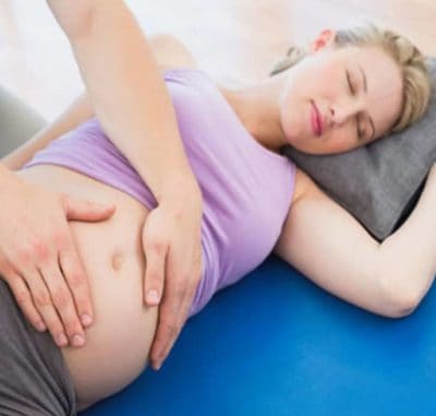 Pregnancy massage pcituredd with specialist therapist with hands on pregnant women's belly for comfort